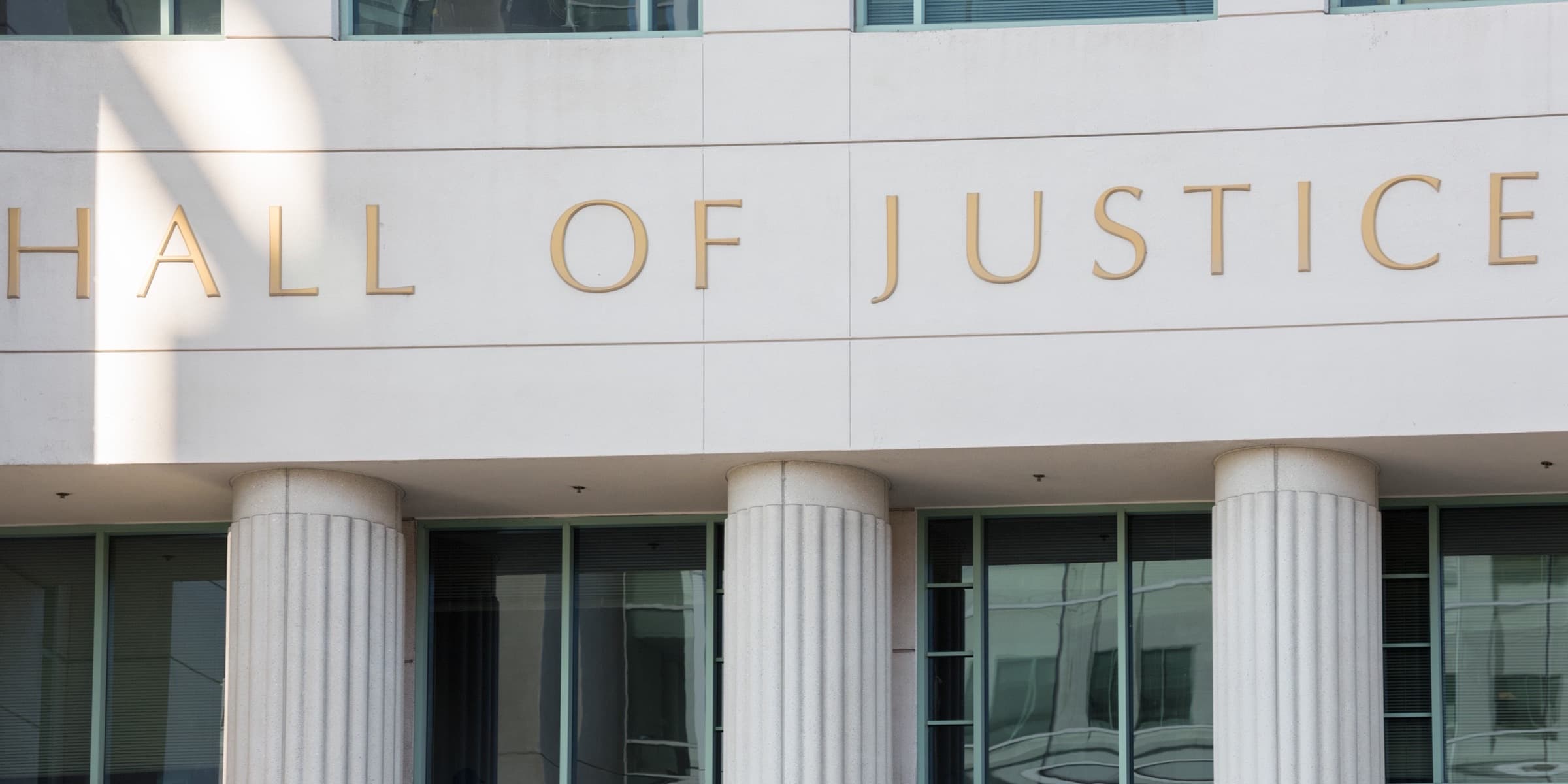 Classical columns and a glass facade with 'Hall of Justice' engraved in gold — illustrative civic imagery representing the practice of law.